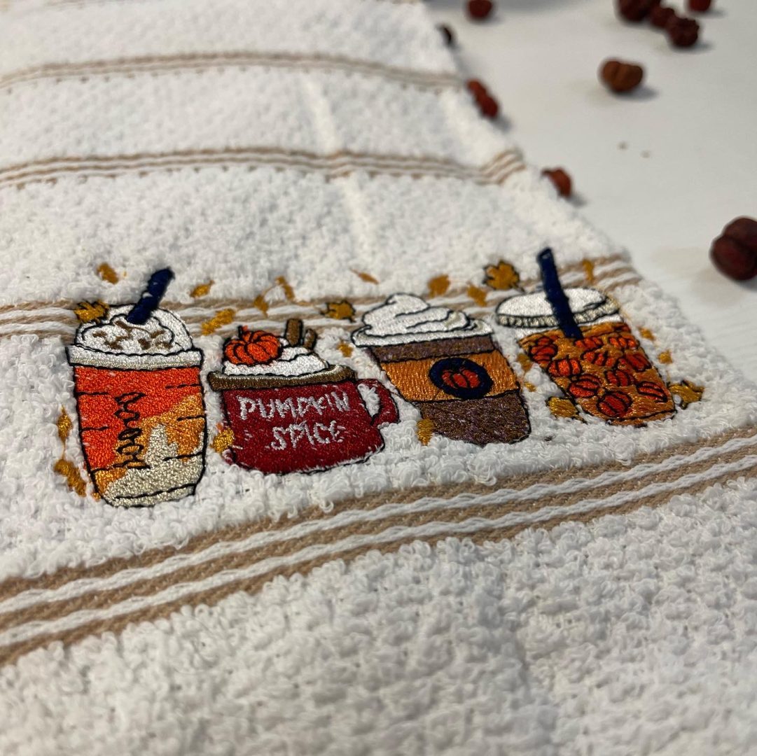 White towel with embroidered pumpkin spice fall coffee drinks and autumn leaves design