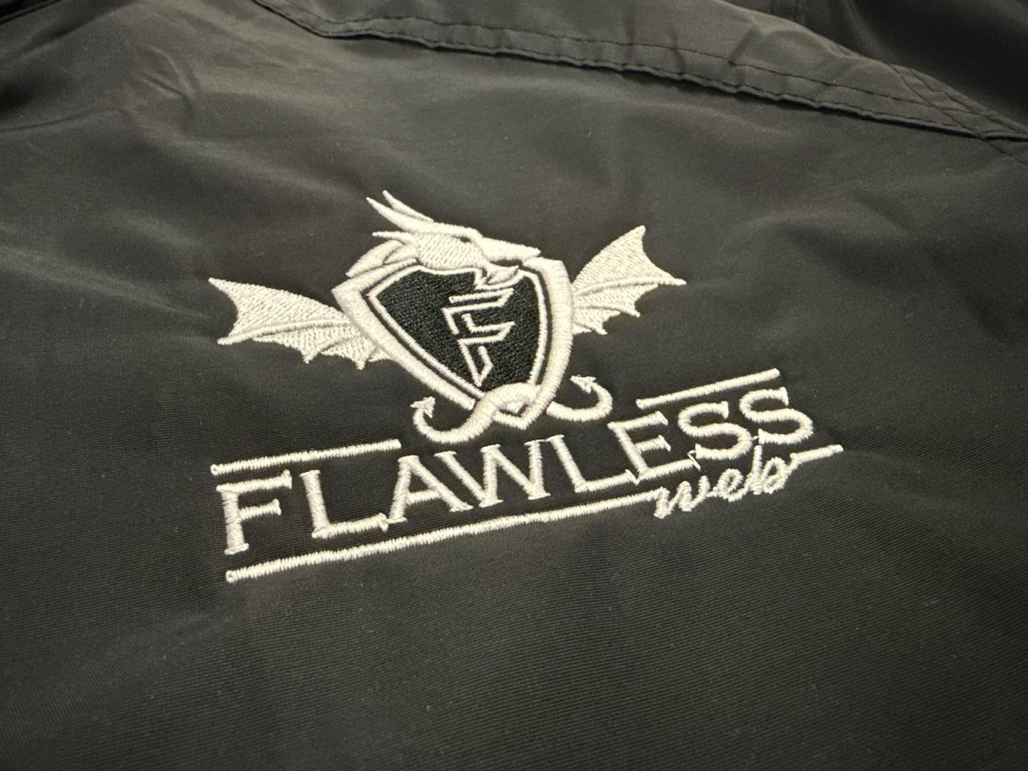 Black jacket with embroidered Flawless Web company logo featuring dragon with shield and wings
