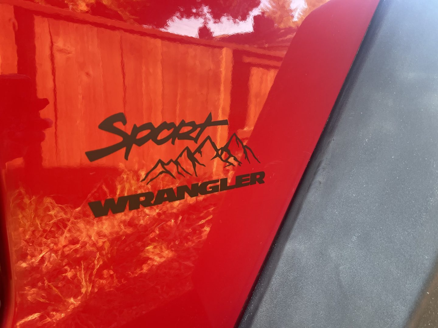 Custom vinyl decal on red Jeep Wrangler Sport fender with mountain silhouette design