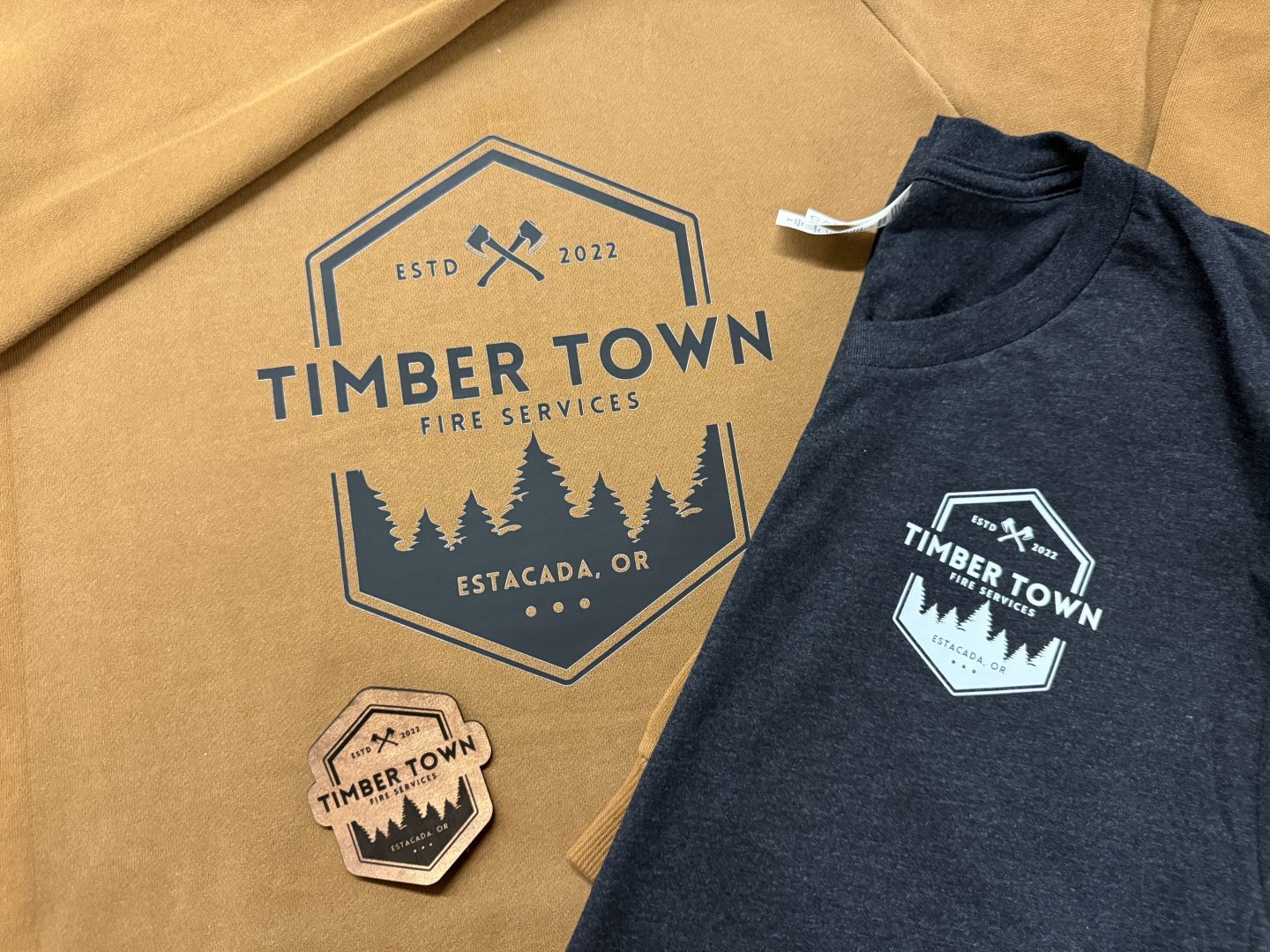 Timber Town Fire Services Estacada Oregon branded apparel tan hoodie charcoal t-shirt with logo and wooden sticker