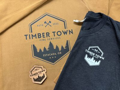 Timber Town Fire Services Estacada Oregon branded apparel tan hoodie charcoal t-shirt with logo and wooden sticker